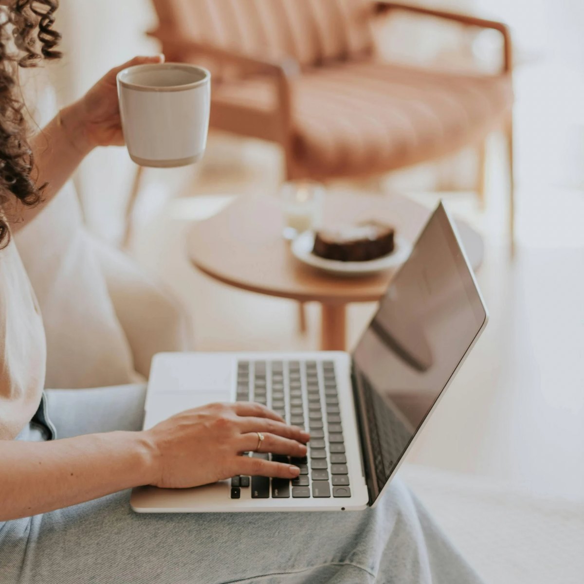 A parent sitting with a laptop on their lap and a mug of coffee in warm afternoon light